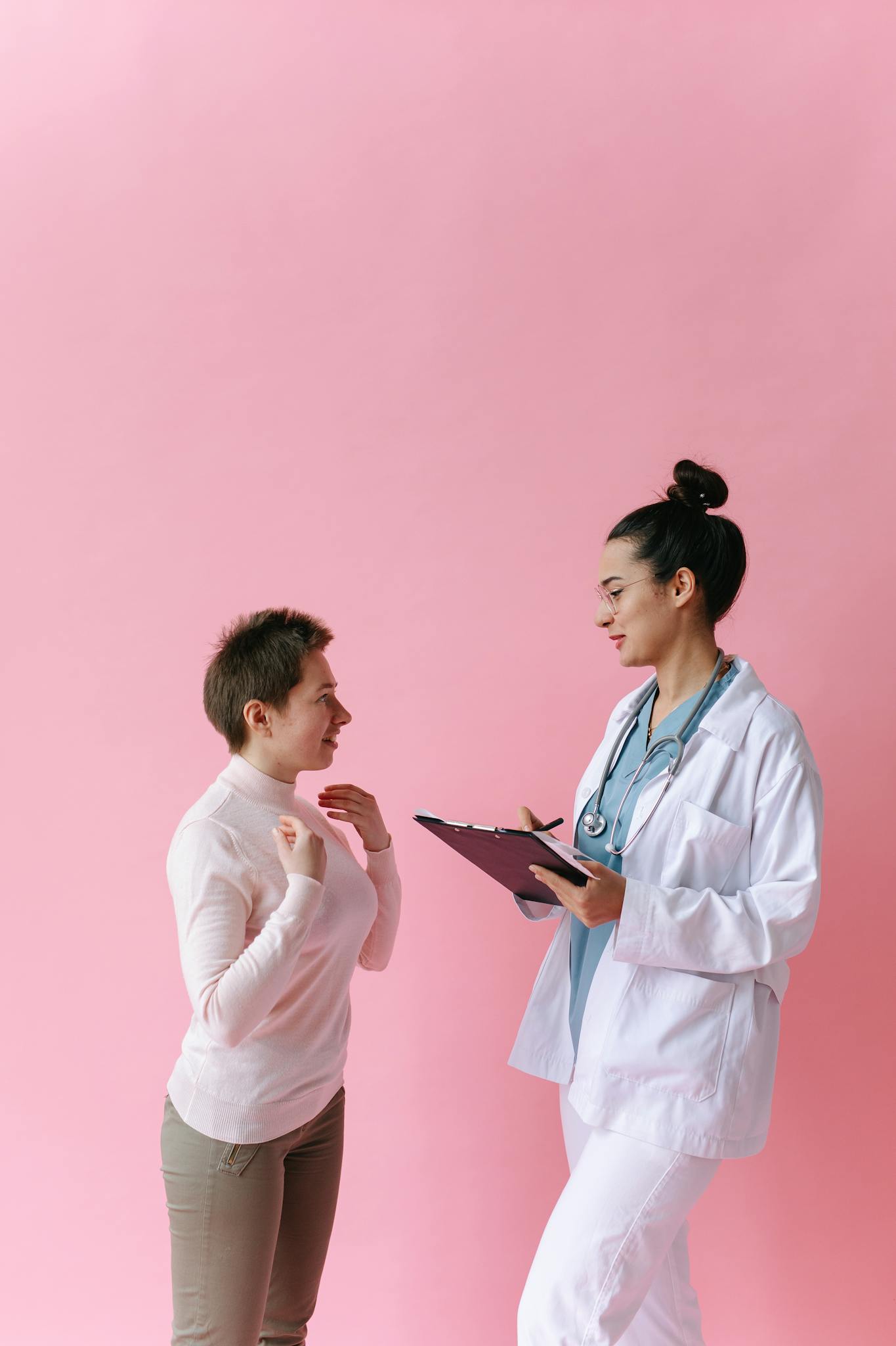 A doctor consults with a patient against a pink background, illustrating healthcare professionalism.
